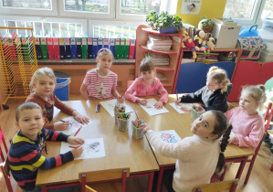 Dzieci siedzą przy stole i kolorują misie.