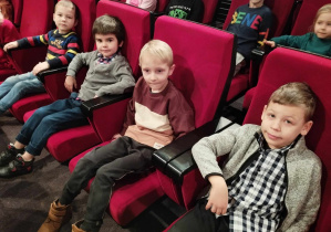 Dzieci siedzą na fotelach w teatrze i pozują do zdjęcia.