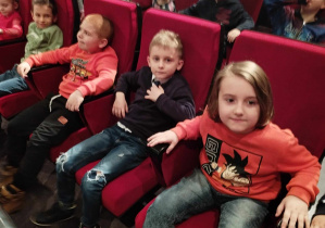 Dzieci siedzą na fotelach w teatrze i pozują do zdjęcia.