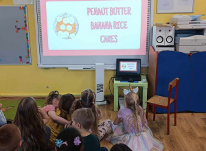 Dzieci siedzą przed tablicą interaktywną i oglądają prezentację.