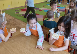 Dzieci siedzą przy stole i jedzą własnoręcznie przygotowane wafle ryżowe z masłem orzechowym i bananem.