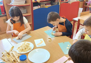 Dzieci siedzą przy stole i kroją banany.