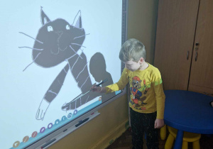 Chłopiec wypełnia kolorem kontur kota na tablicy interaktywnej