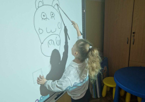 Dziewczynka rysuje na tablicy interaktywnej sylwete kota