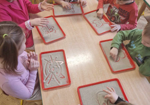 Dzieci rysują palcem na tackach z piaskiem kotka