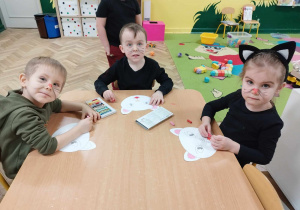 Dzieci malują pastelami papierowe głowy kotów