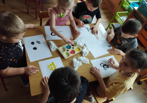 Dzieci siedzą przy stole i malują palcami.