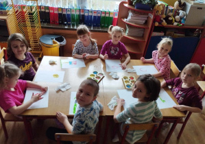 Dzieci siedzą przy stole i malują palcami ulubione zabawki.