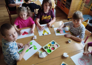 Dzieci siedzą przy stole i malują palcami ulubione zabawki.
