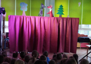 Dzieci oglądają przedstawienie teatralne przed nimi kukiełką lisa i wilka