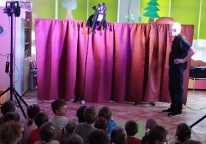 Dzieci oglądają przedstawienie teatralne przed nimi aktor i kukiełka kota