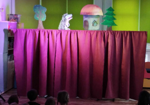 Dzieci oglądają przedstawienie teatralne przed nimi kukiełka jeża i jego domek