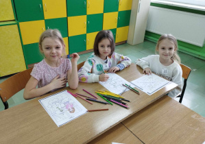 Dzieci siedzą przy stole i kolorują malowanki