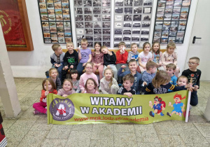 Dzieci pozują do zdjęcia trzymając baner Akademii malego podróżnika