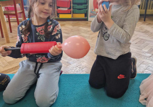 Dziewczynka i chłopiec próbują napompować balony za pomocą ust i pompki