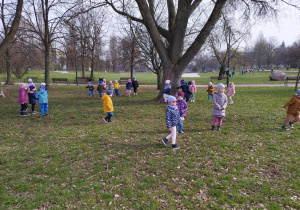 Dzieci z gr 2 i 3 biegają na terenie zielonym w parku